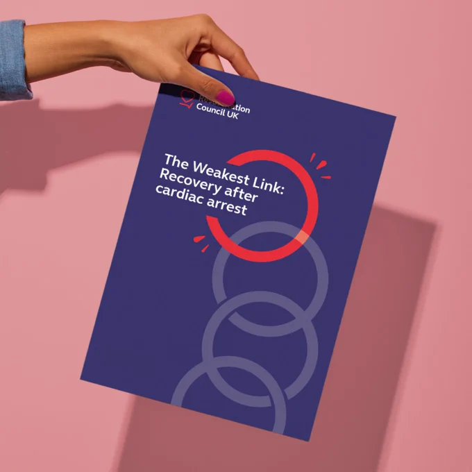A hand holding a report from the Resuscitation Council UK titled "The Weakest Link: Recovery after cardiac arrest" against a pink background. 