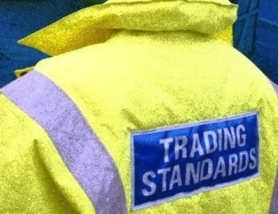 Back of a yellow high-visibility jacket with "TRADING STANDARDS" written on a blue patch.