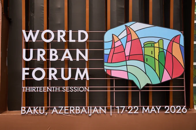 Signage for the World Urban Forum Thirteenth Session displayed at the event venue. The installation features large white lettering alongside a colorful forum logo, with text indicating the location and dates: Baku, Azerbaijan, 17–22 May 2026.