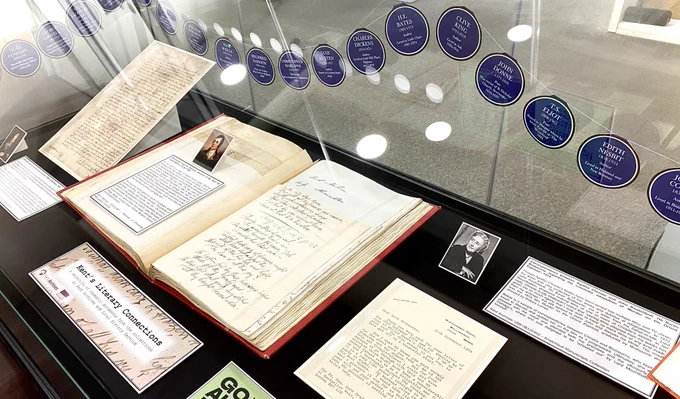 Shown here is a photograph of the left-hand display cabinet outside the Search Room at Kent Archives and Local History Service, Maidstone.

It currently contains a display curated to celebrate the National Year of Reading, including original manuscripts by John Donne, Robert Burns, Agatha Christie and Siegfried Sassoon.

To decorate the cabinet, we’ve added miniature bunting inspired by the blue plaques affixed to buildings that indicate a notable person’s connection to a place. Our plaques shine a spotlight on literary figures and their links to locations across Kent.