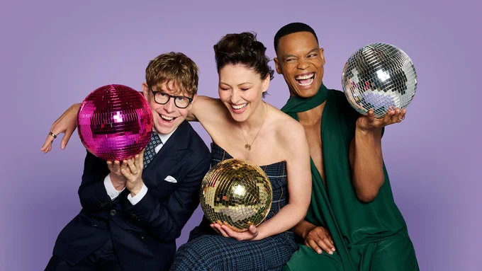 Three people sit smiling and laughing, holding colourful glitterballs