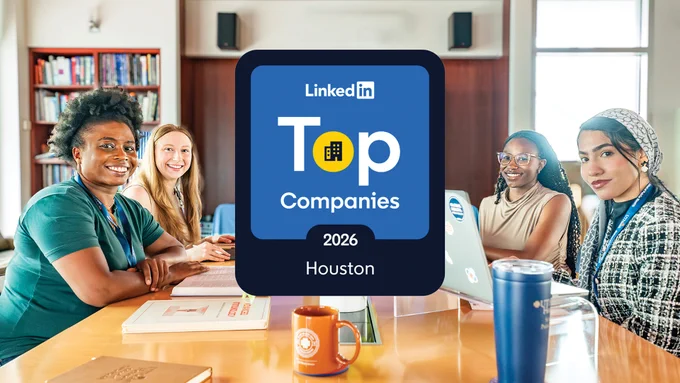 A group of people sitting around a conference table with laptops and notebooks. A plaque on the table reads "LinkedIn Top Companies 2026 Houston." A bookshelf and a window are visible in the background.