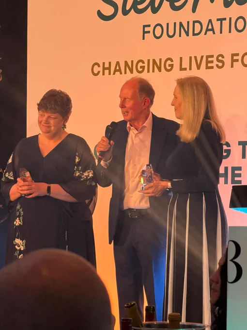 Three people on stage holding awards, with one speaking into a microphone at an awards event.