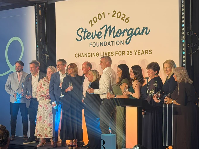 Group of award recipients standing on stage holding trophies beneath a “Steve Morgan Foundation – Changing Lives for 25 Years” backdrop.