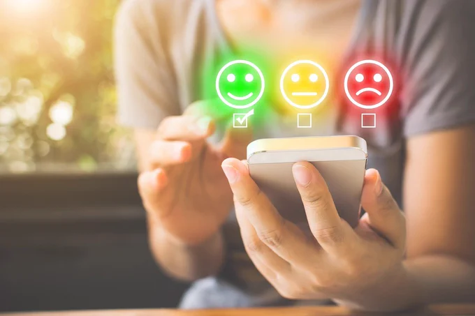 A photo of a young person using a smartphone with three rating smiley faces for good, okay and good reactions for feedback.