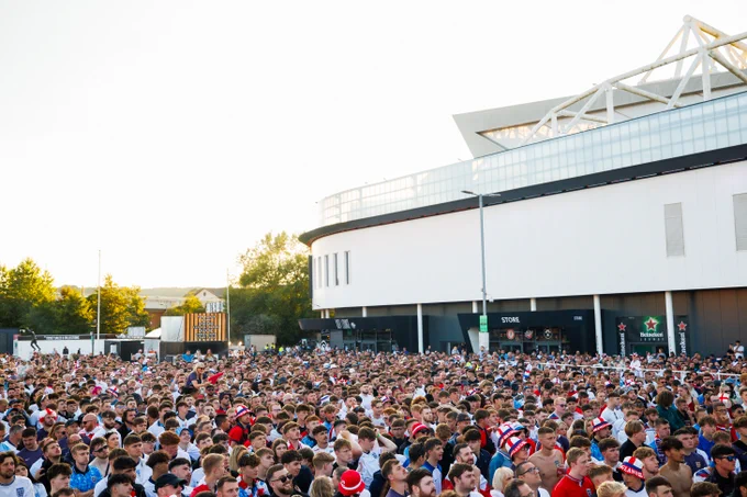 Large crowd of sports fans gathered outside a stadium on a sunny day, many wearing team colors and hats.