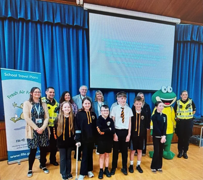 Two police officers with a group of young persons and adult teachers in a school hall.