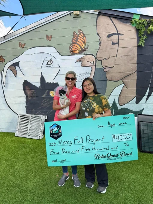 Two women hold a large check for $4,500 in front of a mural featuring a dog and butterflies. They are smiling, suggesting a positive and charitable atmosphere.