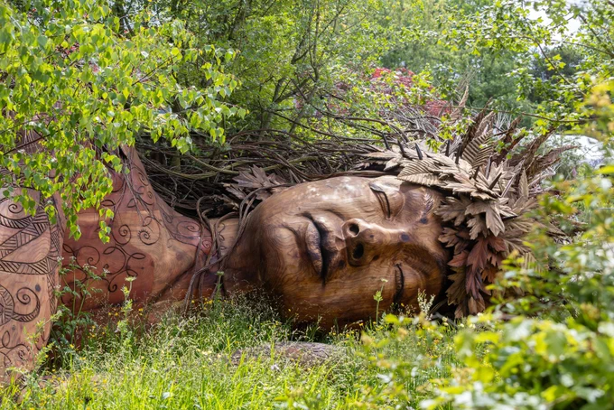 CPRE On The Edge garden at Chelsea Flower Show, with Gaia sculpture resting among trees and plants - photo RHS / Neil Hepworth