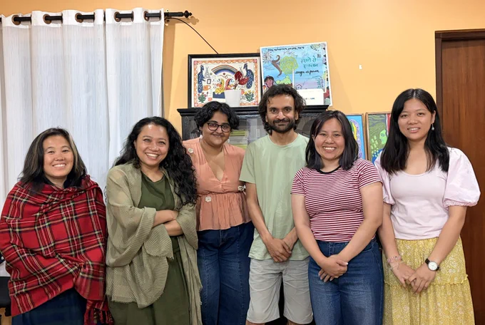 A landscape group picture of six people with a yellow background posing for the picture.