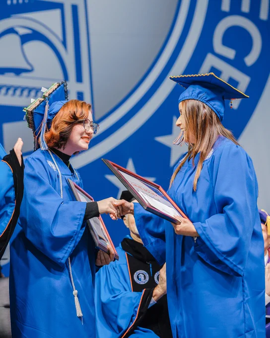 Randolph Community College graduates Bullet Rundberg and Ruth Lambeth shake hands on stage while holding framed awards presented in honor of North Carolina State Auditor Dave Boliek during RCC’s 2026 Commencement Ceremony.