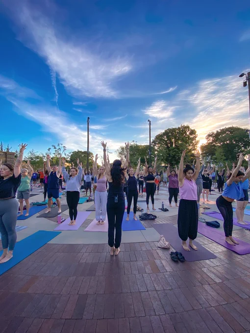Group of people practicing yoga outdoors on mats during a colorful sunset with clear blue sky.