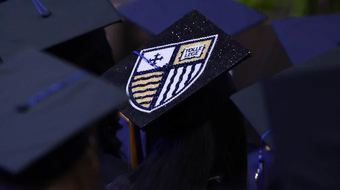 A decorated graduate cap with the Merrimack College shield. 