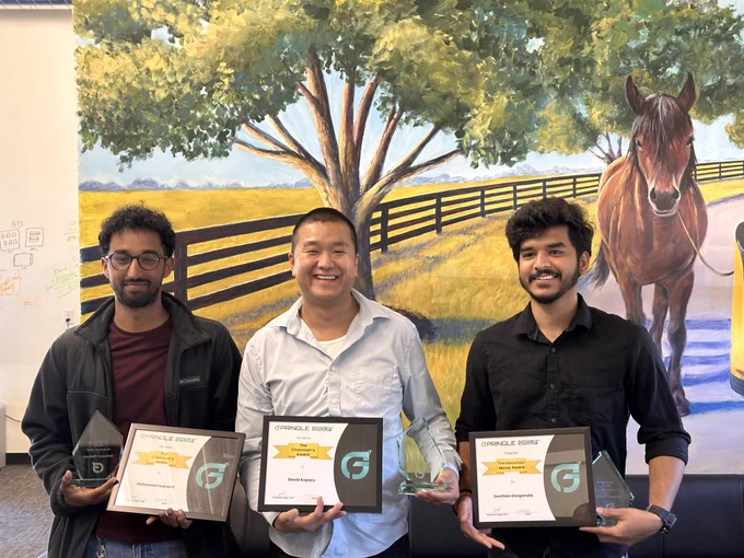Three individuals standing proudly, each holding an award in front of a large mural depicting a tree and a horse. They appear happy and accomplished.