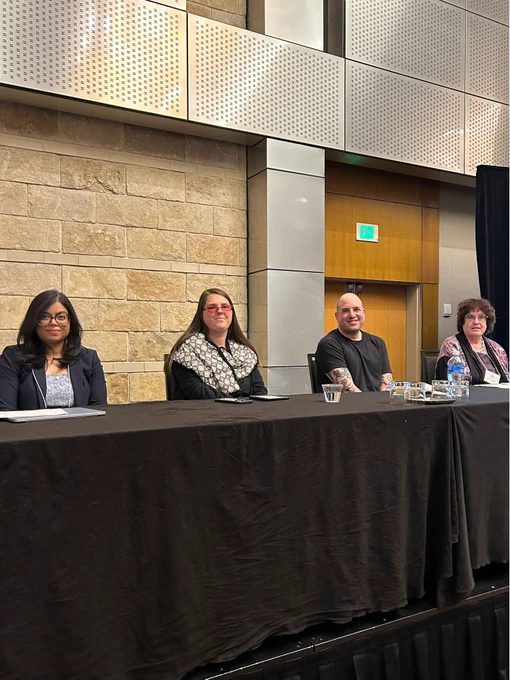 Four panelists sit behind a table. End ID.