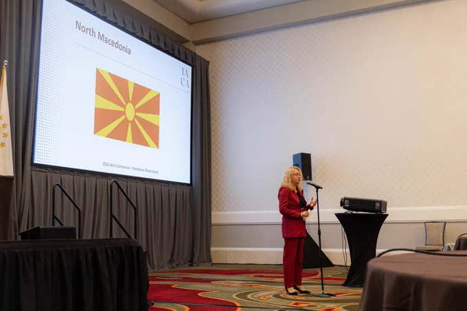 Woman speaking at a microphone with screen behind her, with "North Macedonia" title and flag