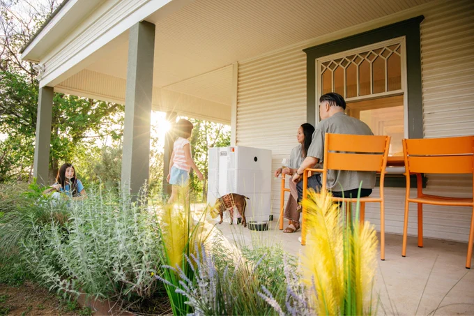A family sits outdoors on a patio near a Base Power battery at a home.