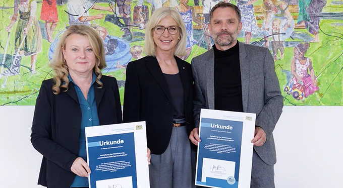 Das Bild zeigt Bayerns Sozialministerin Ulrike Scharf bei der Übergabe des Prädikates „Landesfachstelle Barrierefreiheit“ an Prof. Lydia Haack, Präsidentin der Bayerischen Architektenkammer und Thomas Lenzen von der Bayerischen Architektenkammer.