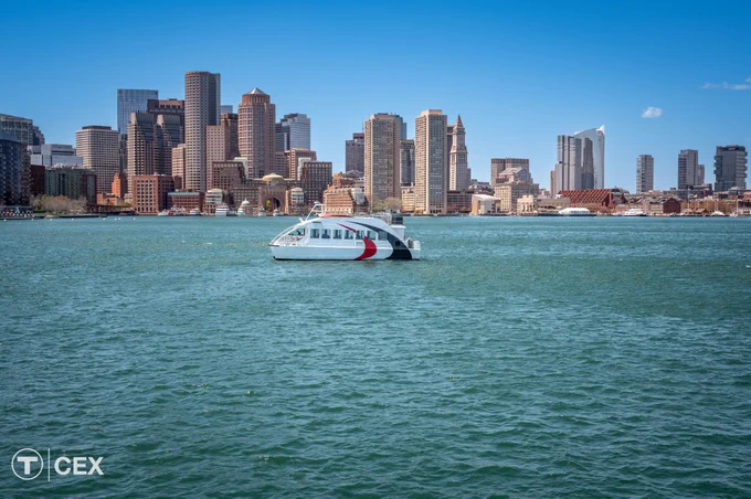 A small ferry boat crossing Boston Harbor with the city skyline in the background.