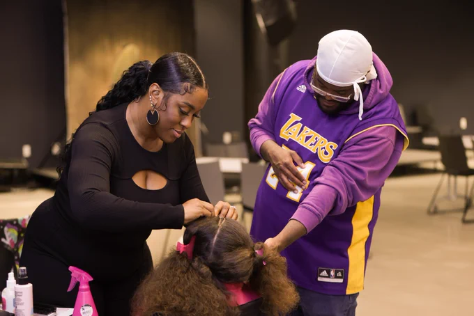 A father helping with his daughter as she gets her hair styled.