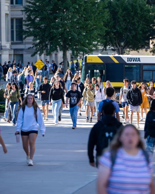 Students at the University of Iowa walk through campus between classes on sunny day. (Hint: Herky is near the Cambus)