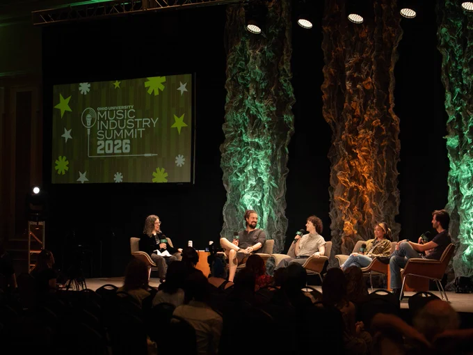 A sign reads, "Ohio University Music Industry Summit 2026," as keynote panelists speak seated on stage, with green and orange lights behind them.