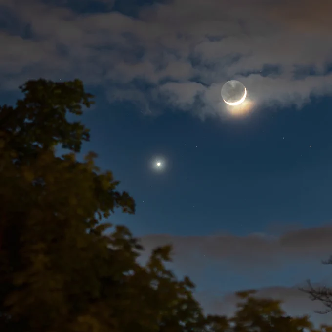 Bright, star-like Venus in the late dusk sky near the thin crescent Moon glowing amid the clouds. Photo: NASA/Bill Dunford