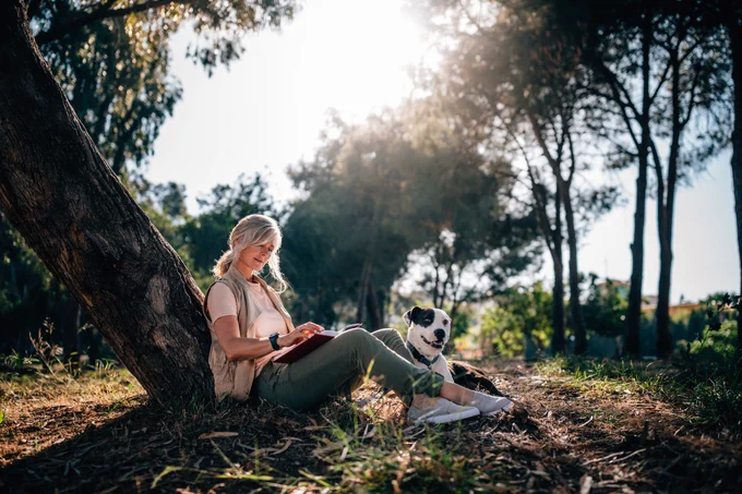 A woman sits underneath a tree with her dog.