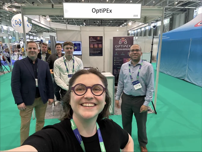 Image shows six people at a stand for the OptiPEx project at an exhibition.