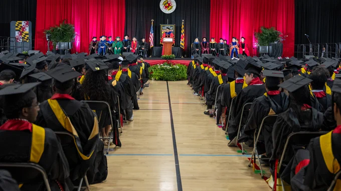View from the back of the graduate commencement ceremony, with the audience full of graduates in regalia and Dean Amitabh Varshney standing at the lectern speaking