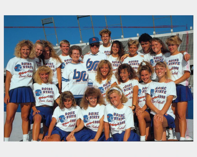 Boise State students from the 90s smiling together wearing matching shirts that say "Boise State 1990 Bronco Football" on The Blue. 
