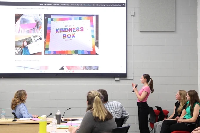 NHS Officer speaking into a microphone as they present their project that is shown on a large TV screen