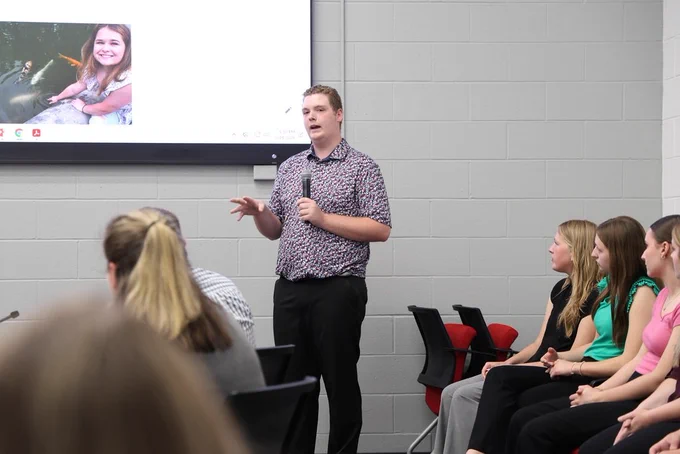 NHS Officer speaking into a microphone as they present their project that is shown on a large TV screen
