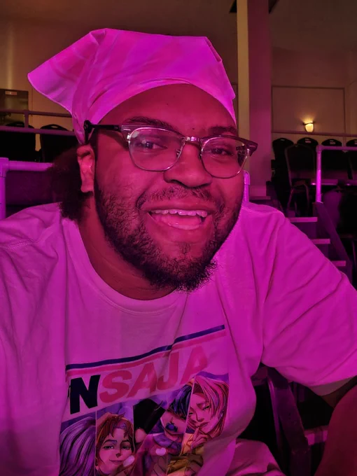 A selfie of me. Im smiling and wearing glasses. I'm coated in a pink light.