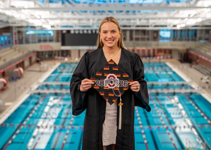 Lena inside the aquatics center on top of the highest diving platform, she's holding up her cap with is bedazzled with the Ohio State logo, "2026" and German flags