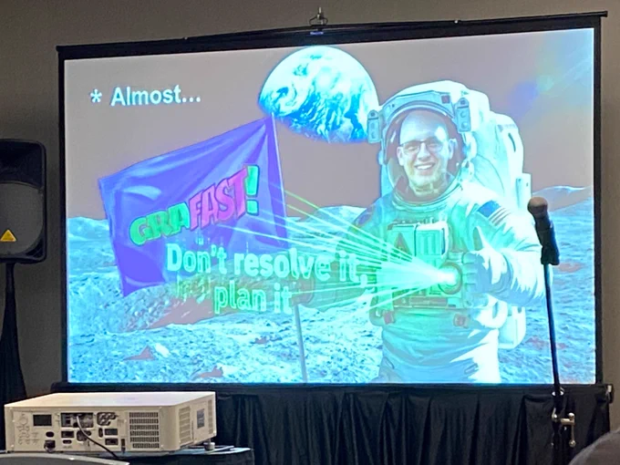 The slide is an AI generated image of Benjie as an astronaut on the moon, holding a Grafast flag and projecting the phrase “dont resolve it, plan it” with a laser 
