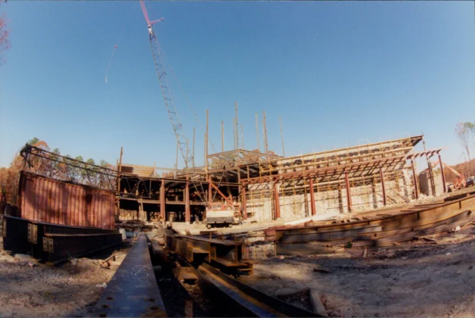 A construction site featuring a large, partially built structure with metal beams and a crane. 