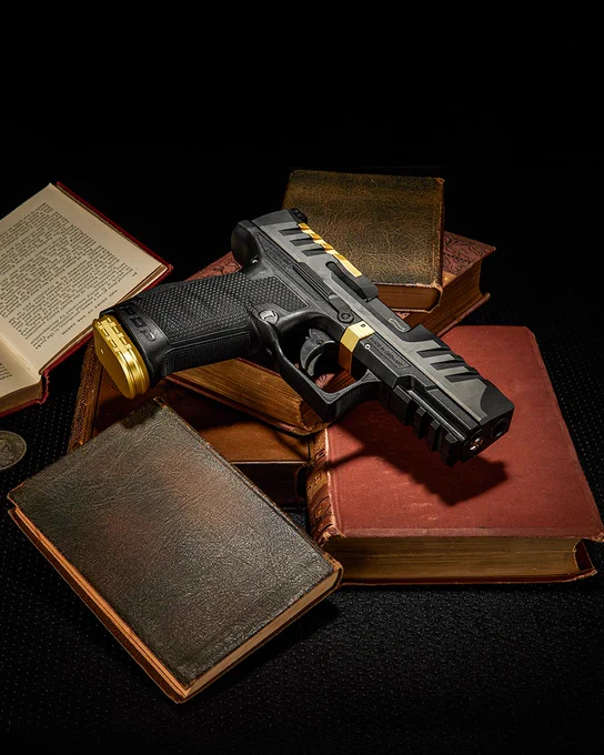 Wide composition of black and gold machined components arranged on stacked vintage books in a dark studio setting.