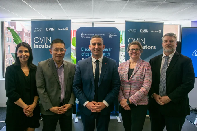 Five people stand together in front of three banners inside the U of T Engineering Partnerships office, with one OCI/OVIN/Ontario banner on each side and a U of T Engineering Partnerships banner in the middle.