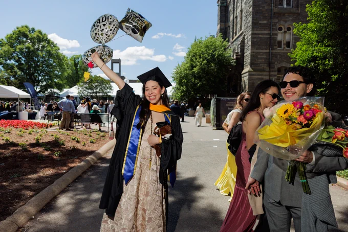 A graduating student holds a bundle of balloons aloft while smiling into the camera.