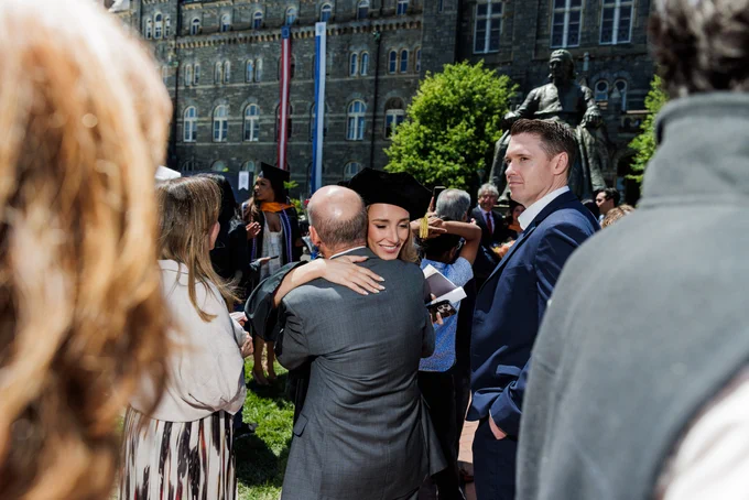 A recent graduate embraces a family member in front of Healy Hall and a statue of John Carroll.