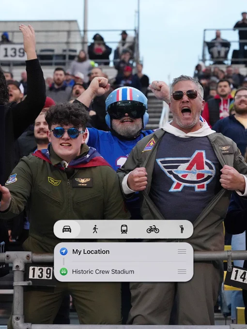 Excited fans, dressed in themed outfits, cheer energetically at a stadium. A navigation banner is visible in the foreground.
