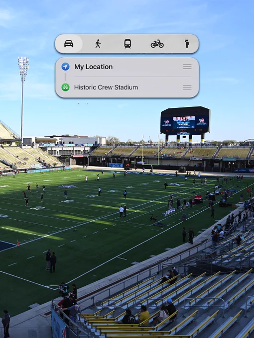 A large empty sports stadium is shown with a digital overlay indicating directions to 'Historic Crew Stadium.' The bright, sunny day creates a calm atmosphere.