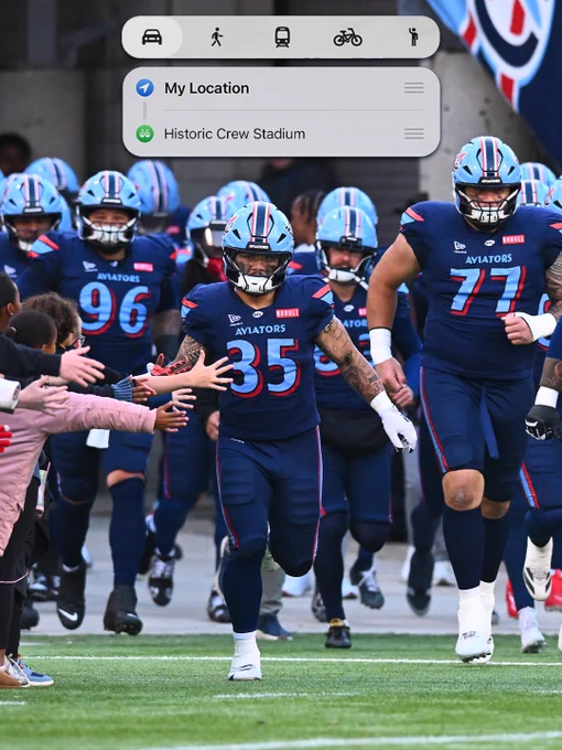 Football players from the Aviators team enter a stadium, high-fiving fans. The mood conveys energy and anticipation.