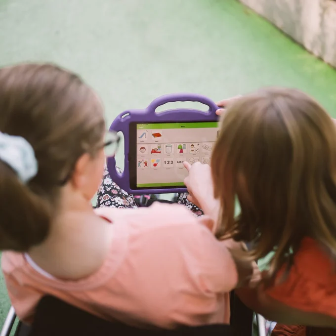 AAC communication app in use on a purple-cased tablet. A child points to digital icons, illustrating specialized digital accessibility tools.