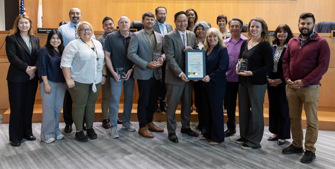 People standing in the Contra Costa County Board of Supervisors chamber, displaying awards and a proclamation