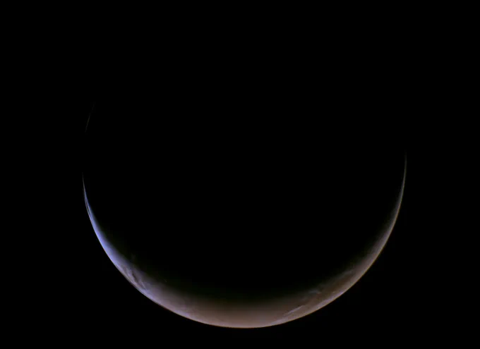 A crescent-shaped Mars against the darkness of space. Within the thin illuminated crescent, the reddish surface and some clouds can be seen. 