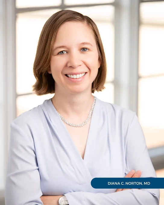 Dr. Diana Norton of Tryon Medical Partners smiles with her arms crossed in a professional portrait posed in front of a paned glass window