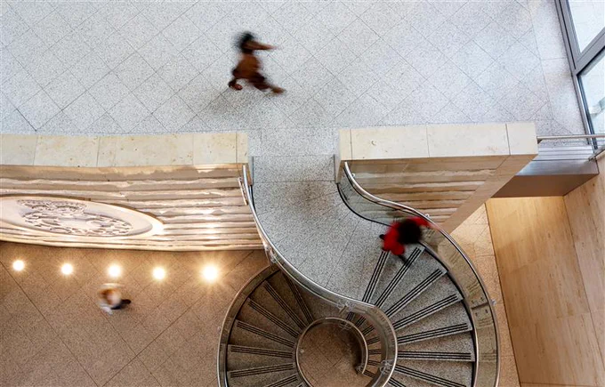 Overhead view of three individuals walking around a spiral staircase in GCHQ's HQ with a detailed tile floor.