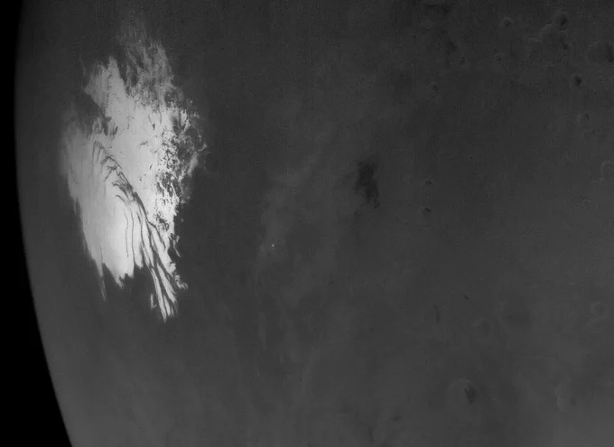 Black-and-white photo of the south polar ice cap of Mars. The cap has swirling layers of white ice on a vast, mostly flat plain.